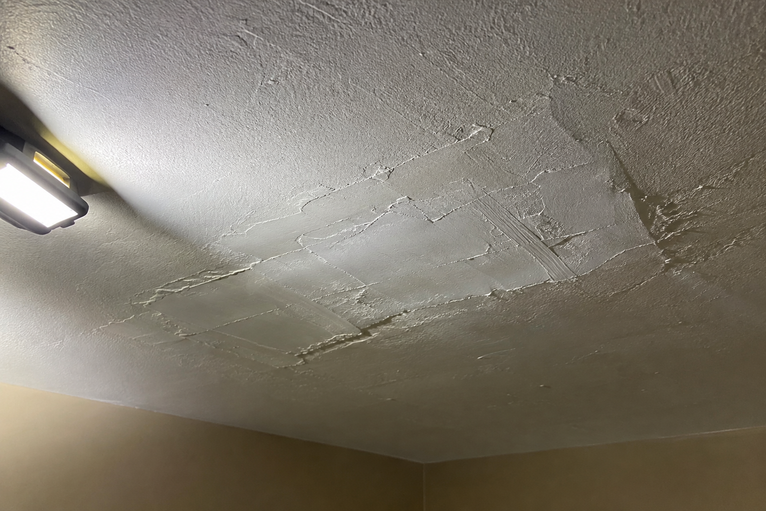 Work light raking across a fresh joint compound patch on a ceiling, showing its ridges, in Riverside, CA